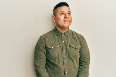 Gündelik kıyafetler giyen genç latin adam gülümseyip yan tarafa bakıyor ve düşünüyor.. 