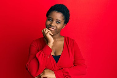Afro saçlı, kırmızı arka planda günlük giysiler giyen genç Afrikalı kadın şüpheye odaklanmıştı. 