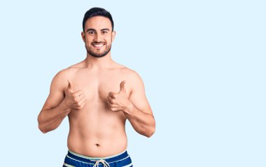 Mayo giyen genç ve yakışıklı bir adam elinde olumlu bir jest yapıyor, gülümsüyor ve mutlu. Neşeli ifade ve kazanan jest. 