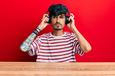 Masada oturan, kafası karışık ve habersiz kulaklık takan genç İspanyol adam. şüphe kavramı. 