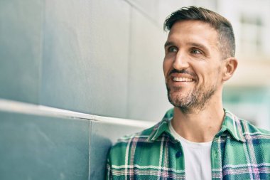 Genç beyaz adam gülümseyerek şehirde mutlu mesut duruyor..