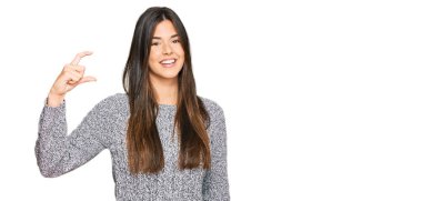 Kış süveteri giyen genç esmer kadın gülümsüyor ve kendine güvenen el hareketleriyle küçük beden işareti yapıyor parmaklarıyla ve kamerayla bakıyor. ölçüm kavramı. 