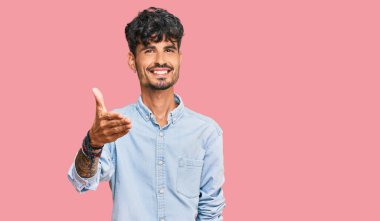 Gündelik kıyafetler giyen genç İspanyol adam dostça bir selamlama ve hoş geldin hediyesi olarak el sıkışmayı sunuyor. başarılı iş. 