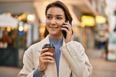 Genç İspanyol kadın gülümsüyor. Şehirdeki akıllı telefondan konuşuyor..