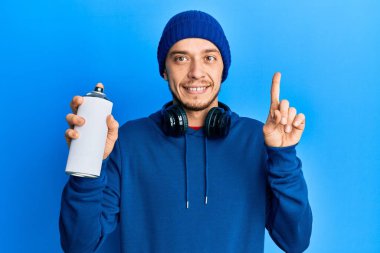 Süveter giyen İspanyol genç adam elinde grafiti spreyi ile gülümsüyor bir fikir ya da soru işareti ile mutlu bir yüz, bir numara 