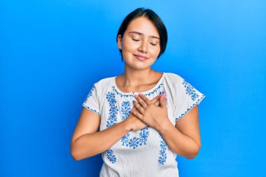 Kısa saçlı, sıradan kıyafetler giyen, göğsünde elleriyle gülümseyen, yüzünde minnet dolu bir jestle gözlerini kapayan güzel bir kadın. sağlık kavramı. 