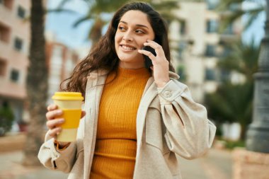 Ortadoğulu genç bir kadın akıllı telefondan konuşuyor. Şehirde kahve içiyor..