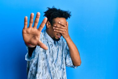 Sakallı, sıradan kıyafetler giyen, elleriyle gözlerini kapatan, üzgün ve korku dolu hareketler yapan Afrikalı genç bir Amerikalı. utangaç ve olumsuz kavram. 
