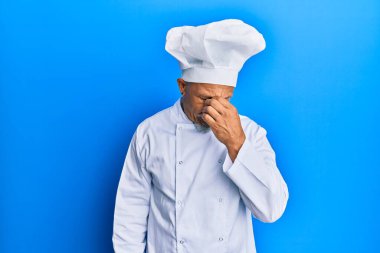 Profesyonel aşçı üniforması giyen, şapkalı, burnu ve gözleri ovuşturmaktan yorgun düşmüş, yorgun ve başı ağrıyan orta yaşlı bir adam. Stres ve hüsran kavramı. 