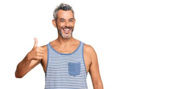 Orta yaşlı, gri saçlı, sıradan giyinen, kolsuz tişörtlü mutlu ve pozitif gülümseyen, başparmağıyla mükemmel ve onay işareti yapan bir adam. 