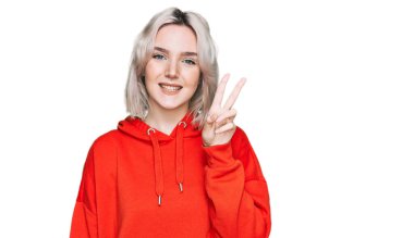 Gündelik kıyafetler giyen genç sarışın kız iki numarayı gösterip işaret ederken kendinden emin ve mutlu bir şekilde gülümsüyor.. 