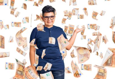 Küçük çocuk günlük giysiler ve gözlük takıyor neşeli bir şekilde gülümsüyor ve avuç içi kameraya bakıyor..