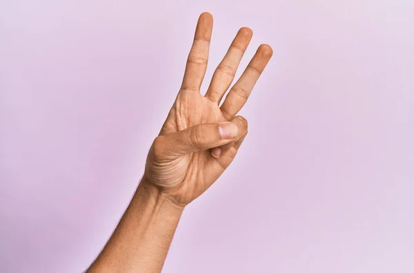 高加索年轻人的胳膊和手在粉色孤立的背景上数着3号 显示出三根手指 — 图库照片