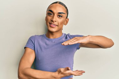 Makyaj yapan, uzun saçlı, sıradan tişörtlü, elleri büyük ve büyük beden işareti olan İspanyol bir adam. Kameraya bakıp gülümsüyor. ölçüm kavramı. 