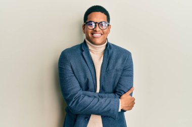 Zarif kıyafetler ve gözlük takan yakışıklı İspanyol adam kameraya bakarken kollarını kavuşturup gülümsüyor. pozitif kişi. 