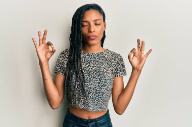 Sıradan kıyafetler giyen, gözleri kapalı gülümseyen, meditasyon yaparken parmaklarıyla gülümseyen Afrikalı Amerikalı bir kadın. yoga konsepti. 
