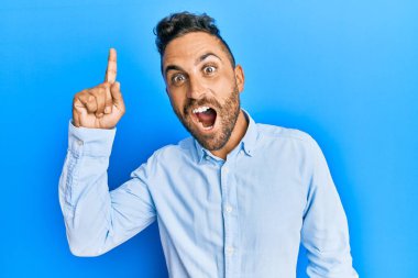 Sıradan kıyafetler giyen sakallı yakışıklı bir adam başarılı bir fikri işaret ediyor. Heyecanlı ve mutlu. Bir numara.. 