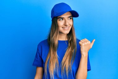 Genç İspanyol kadın teslimat üniforması giyiyor ve şapkalı mutlu yüzlü gülümsüyor başparmağıyla yana bakıyor ve işaret ediyor.. 