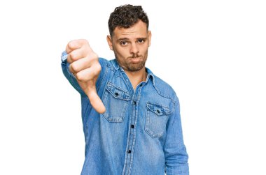 Günlük kot ceket giyen genç İspanyol adam mutsuz görünüyor ve reddediliyor ve olumsuz jestler yapıyor. kötü ifade. 