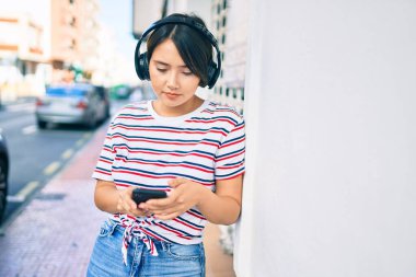 Şehirde akıllı telefon ve kulaklık kullanan ciddi bir suratı olan genç bir Latin kız.