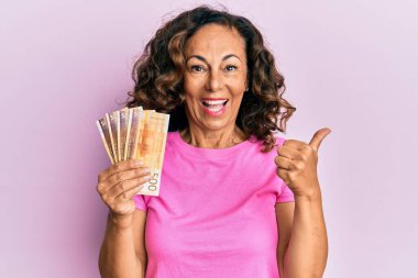 Orta yaşlı İspanyol kadın elinde Norveç kronu banknotları tutarken başparmağıyla ağzını açıp gülümsüyor. 