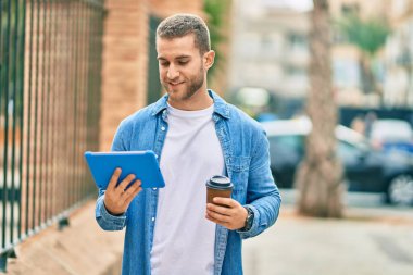 Genç beyaz adam mutlu bir şekilde gülümsüyor dokunmatik ped kullanıyor ve şehirde kahve içiyor..