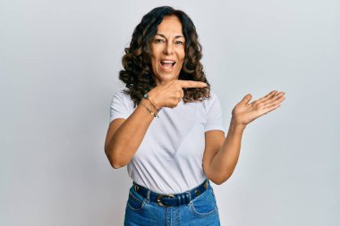 Orta yaşlı, beyaz tişört giyen İspanyol kadın kameraya hayret ediyor ve gülümsüyor.. 