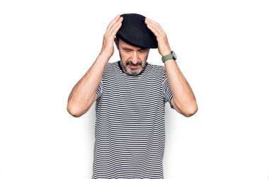 Orta yaşlı yakışıklı bir adam çizgili tişört giyiyor ve beyaz arka planda Fransız beresi takıyor. Elleri başının üstünde, stresten baş ağrısı çekiyor. Migren ağrısı..
