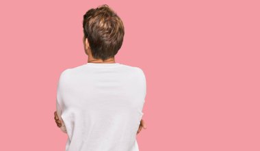 Beyaz bir süveter giyen yakışıklı beyaz bir adam arkasını dönüp kollarını kavuşturarak başka tarafa bakıyor. 