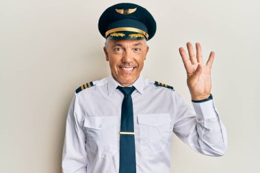 Yakışıklı, orta yaşlı, uçak pilotu üniforması giyen, kendinden emin ve mutlu bir şekilde gülümseyerek dört numarayı gösteren ve işaret eden olgun bir adam.. 