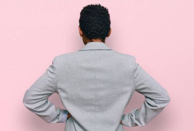 Genç Afro-Amerikan kadın iş kıyafetleri giymiş. Arkaya bakıyor. Kolları vücudunda. 