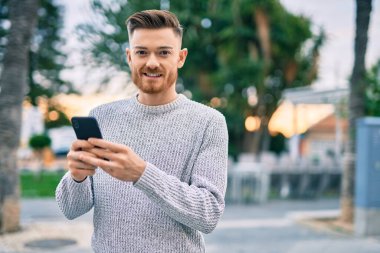 Beyaz adam şehirde akıllı telefon kullanarak mutlu bir şekilde gülümsüyor..