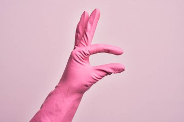 İzole edilmiş pembe arka plan üzerinde temizlik eldiveni olan beyaz bir adamın eli. Görünmez bir şeyi alıp, parmaklarında boşluk gösteren bir nesneyi tutuyor.