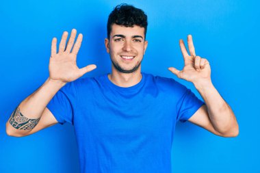 Günlük mavi tişört giyen genç İspanyol adam 8 numarayı gösterip işaret ederken kendinden emin ve mutlu gülümsüyor.. 