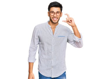 Gündelik kıyafetler giyen, gözlüklü, gülümseyen, kendine güvenen, el hareketi yapan, parmaklarıyla işaret yapan ve kameraya bakan genç yakışıklı bir adam. ölçüm kavramı. 