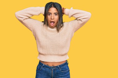 Kışlık yün kazak giyen genç Latin kız çıldırmış ve elleri başının üstünde korkmuş, korkmuş ve ağzı açık şoktan şaşırmış. 