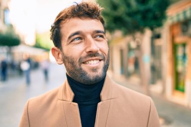 Zarif ceket giyen yakışıklı iş adamı dışarıda mutlu bir şekilde gülümsüyor.