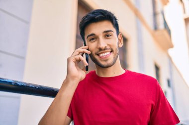 Genç Latin adam gülümsüyor ve şehirde akıllı telefondan konuşuyor..