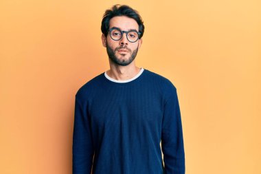 Yüzünde ciddi bir ifade olan günlük kıyafetler ve gözlük takan genç İspanyol bir adam. Basit ve doğal bir şekilde kameraya bakıyorsun.. 