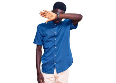 Genç, Afro-Amerikan bir adam günlük kıyafetler giyiyor. Gözleri kollarıyla kapatıyor, ciddi ve üzgün görünüyor. Görme, saklama ve reddetme konsepti 