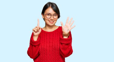 Kısa saçlı, sıradan süveter giyen, gözlüklü, 6 numaralı parmaklarıyla işaret eden, kendinden emin ve mutlu gülümseyen güzel İspanyol bir kadın.. 