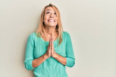 Güzel sarışın kadın, sıradan bir kazak giyip elleri bağlı yalvarıyor ve dua ediyor. Yüzünde umut ifadesi var. Çok duygusal ve endişeli. Yalvarıyor. 