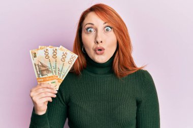 500 Norveçli kronu elinde tutan güzel kızıl saçlı kadın. Korkmuş ve şaşkın bir şekilde ağzı açık kalmış, inançsız bir yüz. 