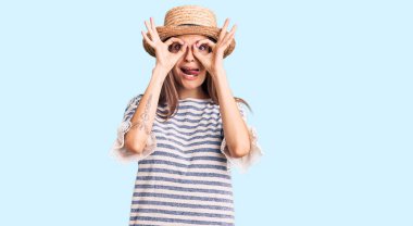 Güzel beyaz kadın yaz şapkası takıyor dürbün gibi jest yapıyor, gözleri parmaklarından bakıyor. çılgın ifade. 