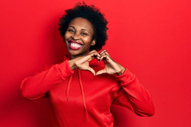Sıradan bir eşofman üstü giyen genç Afro-Amerikan kadın. Sevgiyle gülümseyen, elleriyle kalp sembolü yapan. romantik kavram. 