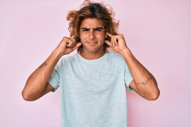 Gürültülü müzik sesi için günlük kıyafetler giyen genç İspanyol adam kulaklarını parmaklarıyla kapatıyor. sağır kavramı. 