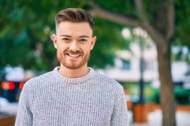 Genç beyaz adam parkta mutlu bir şekilde gülümsüyor..