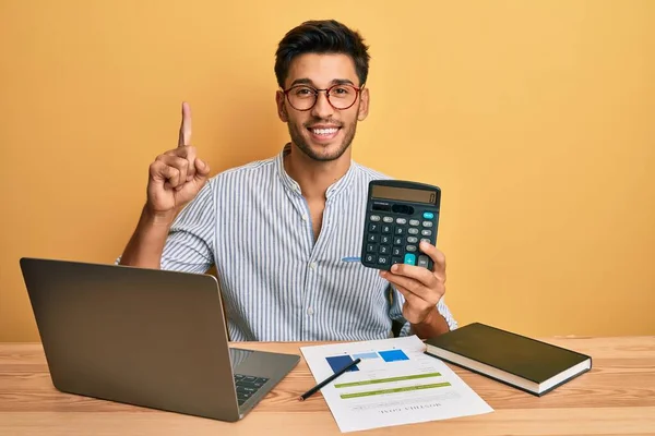 Młody Przystojny Latynoski Mężczyzna Pomocą Kalkulatora Komputera Uśmiechnięty Pokazując Liczbę — Zdjęcie stockowe