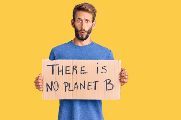 Handsome blond man with beard holding there is no planet b banner scared and amazed with open mouth for surprise, disbelief face