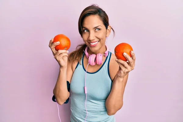 Mujer Latina Joven Usando Ropa Gimnasio Usando Auriculares Sosteniendo Naranjas —  Fotos de Stock